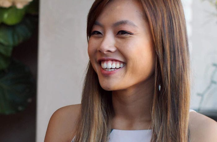 Une jeune femme expose un grand sourire en regardant quelque chose derrière l’appareil photo, montrant ses belles dents blanches.