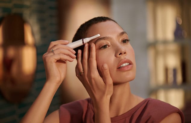 Une femme brune aux yeux marrons utilise la tondeuse-stylo Philips pour épiler ses sourcils.