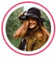 Image de profil d’une consommatrice, une femme rousse sourit et porte un chapeau noir.