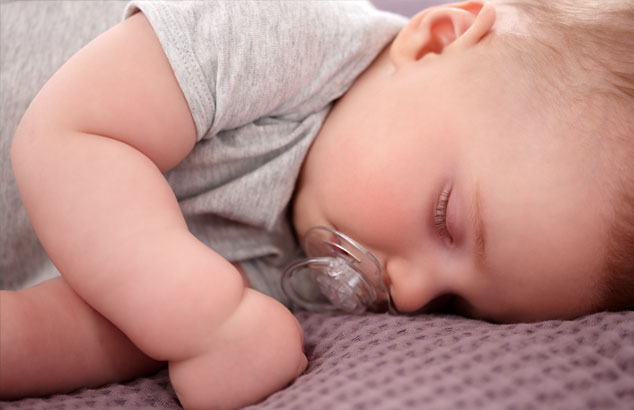 Un bébé avec une tétine transparente sans motif dort sur le côté avec une couverture violette.