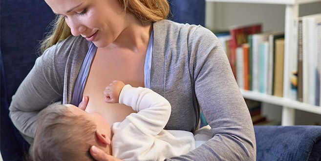 Une mère montre la position de la berceuse modifiée, allaitant tout en soutenant son bébé avec un bras et sa poitrine avec l’autre.
