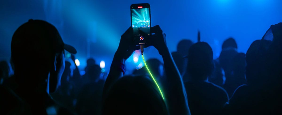 Une personne levant un téléphone portable connecté à un câble lumineux au milieu d'une foule, capturant l'instant présent pendant un événement