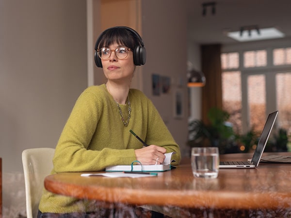 Une personne portant des écouteurs Philips confortables est assise à une table avec un carnet et un ordinateur portable