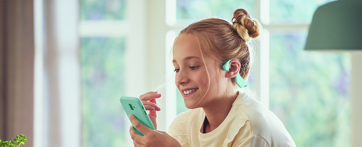 Une fille utilisant un casque vert à conduction osseuse pour enfants