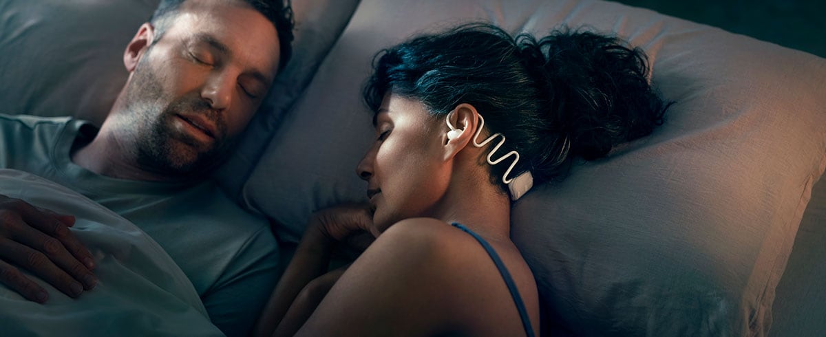 Femme dormant avec son mari, portant un casque spécial sommeil Philips N7808 avec Kokoon