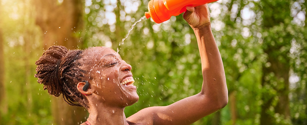 Femme se rafraîchissant en versant de l’eau sur sa tête tout en portant des écouteurs de sport Philips en extérieur
