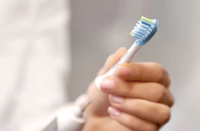 Une personne est en train de rattacher la tête de sa brosse à dents électrique blanche. 
