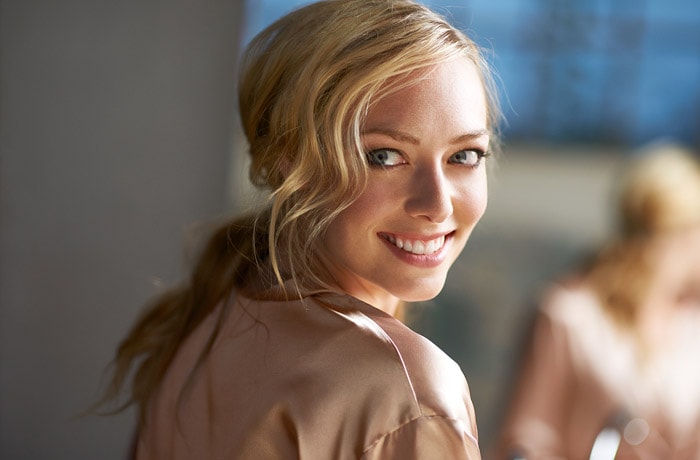 Une jeune femme est tournée vers la caméra, elle regarde de côté tout en souriant, révélant la blancheur éclatante de ses dents. 