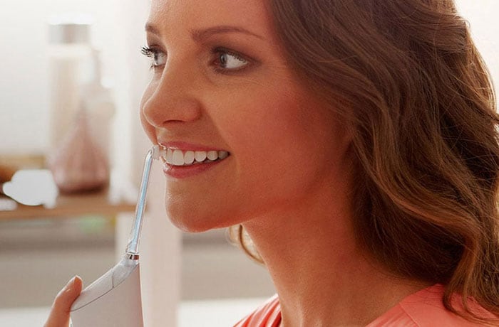 Une femme détourne le regard de la caméra et brosse ses dents blanches à l’aide de la brosse à dents électrique Philips Sonicare Airfloss. 