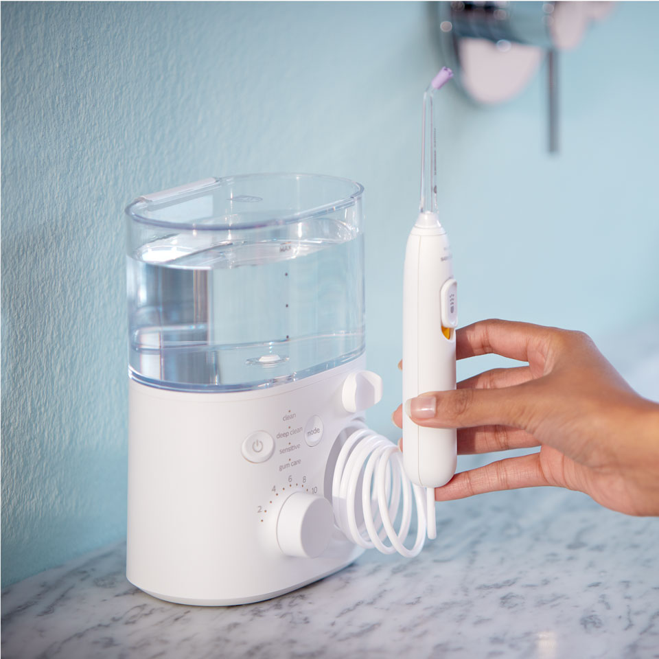 Une main tendue vers un appareil Power Flosser posé sur un plan de travail