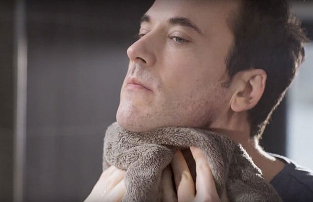 Un homme sèche son cou avec une serviette après le rasage.