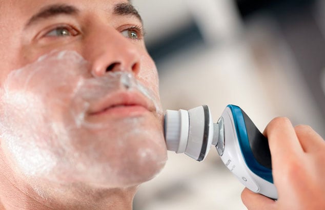 Gros plan sur le visage d'un homme avec de la mousse à raser sur le visage en utilisant une brosse électrique contre sa joue.