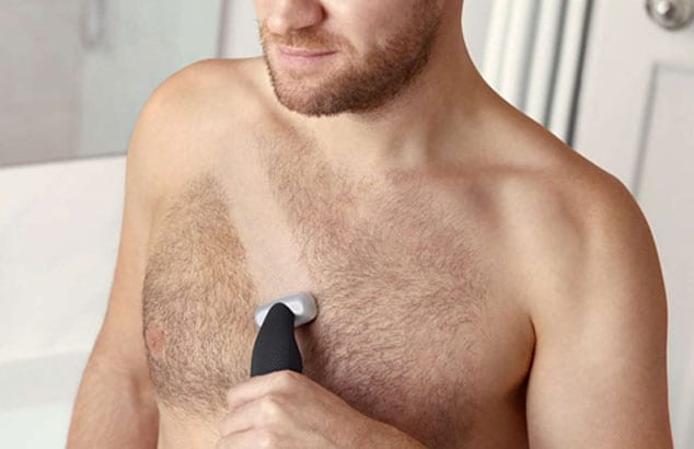 Gros plan sur la poitrine velue d'un homme avec une bande rasée par un rasoir électrique qu'il tient.