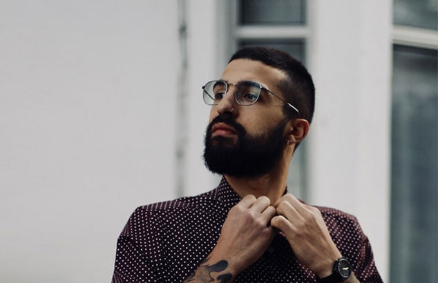 Un homme avec une barbe complète boutonne le haut de sa chemise.