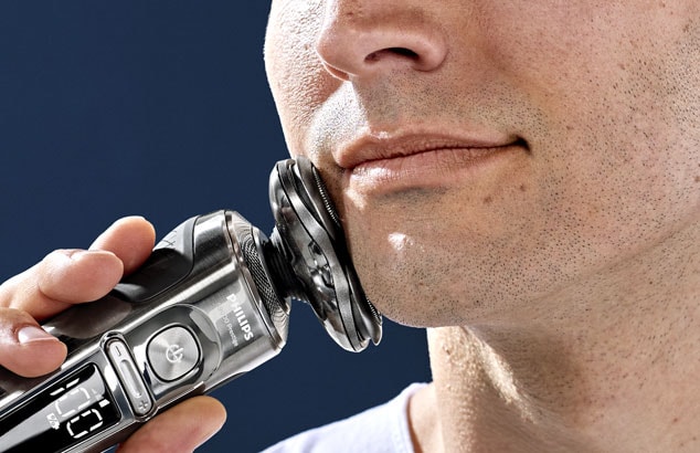 Gros plan sur le menton d'un homme avec une barbe très courte pressant un rasoir électrique contre sa mâchoire.