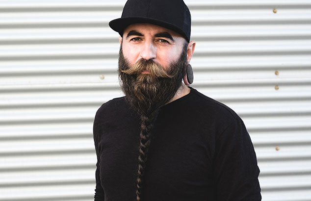 Un homme avec une barbe viking tressée, portant des vêtements noirs, regarde la caméra.