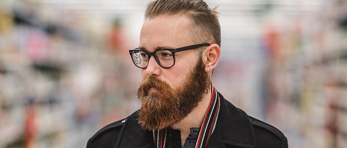 Homme aux cheveux courts et à la barbe bien taillée portant des lunettes noires devant un arrière-plan flou de magasin.