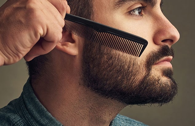 Profil d’un homme avec une barbe complète qui se fait peigner les poils sur les joues.