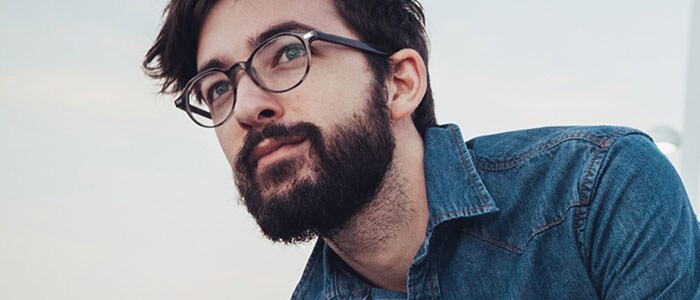 Un homme aux cheveux foncés, portant une chemise en jean et une barbe épaisse.