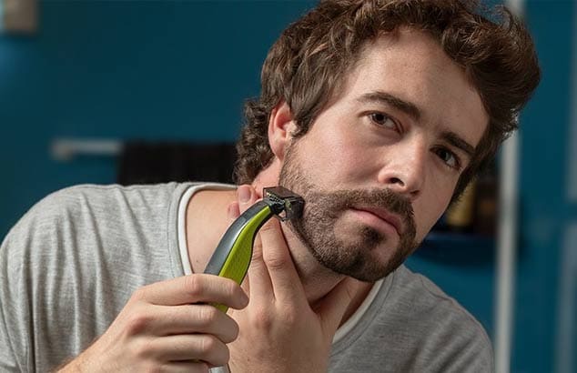 Visage d’un homme en train de tailler la barbe de sa joue avec le Philips OneBlade.