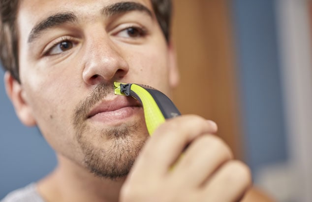 Homme aux cheveux et aux yeux bruns utilisant Philips OneBlade pour façonner la coupe de sa moustache au-dessus de ses lèvres.