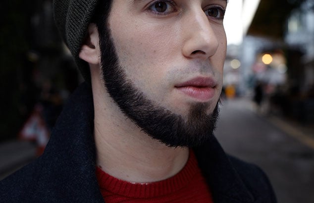 Homme blanc portant un bonnet et un pull rouge avec une barbe de mentonnière foncée très précisément coupée.