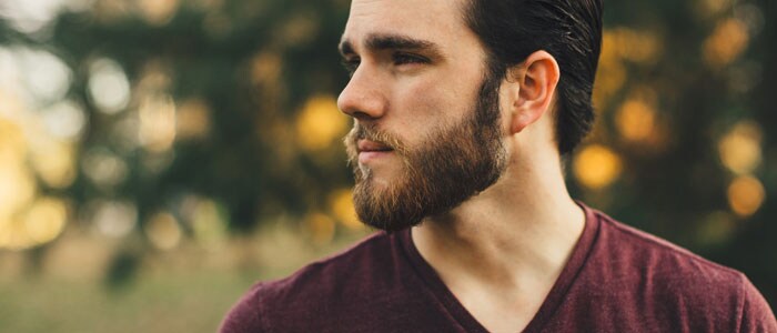 Homme portant une chemise rouge et une barbe regardant sur le côté devant un fond de nature.