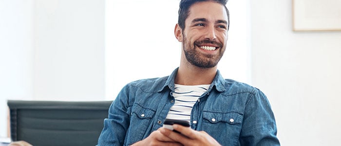 Un homme portant une chemise à barbe tient un téléphone tout en souriant.