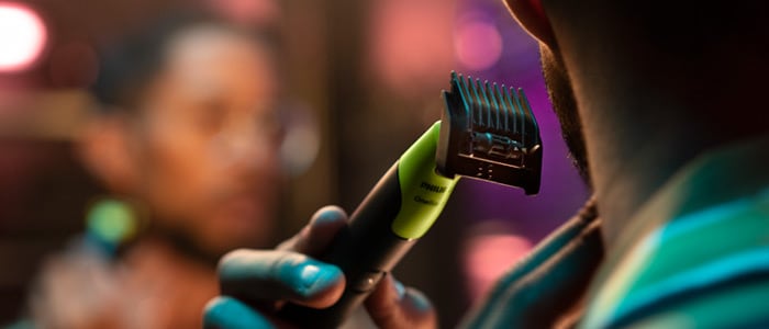 Un homme devant un miroir en train de tracer les contours de sa barbe sur le cou et la nuque à l'aide d'un rasoir Philips OneBlade.