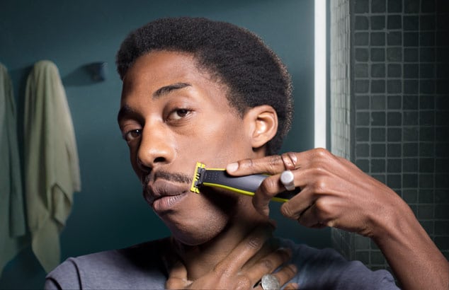 Un jeune homme se taille la moustache avec son Philips OneBlade devant un miroir dans sa salle de bain.