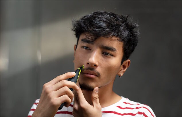 Un jeune homme portant un t-shirt rayon rouge et blanc se taille la moustache avec le Philips OneBlade.