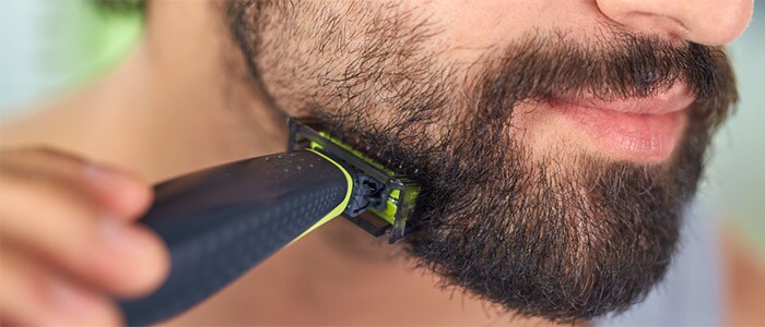 Homme aux yeux bruns en gros plan se taillant la barbe foncée avec le Philips OneBlade.