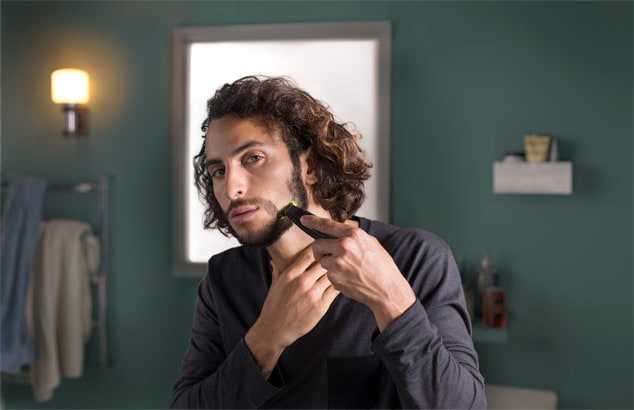 Un homme dans une salle de bain en train de dessiner sa barbe au niveau de la mâchoire avec un rasoir Philips OneBlade.