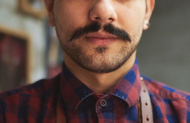 Gros plan sur le bas du visage d’un homme avec une moustache et un bouc court.