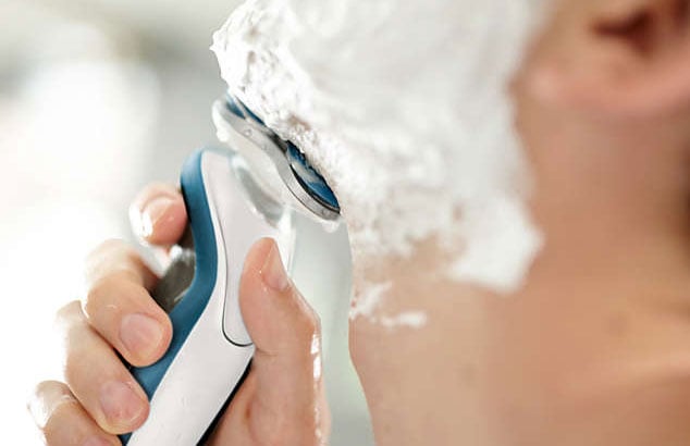Un homme se rase avec un rasoir électrique étanche et de la mousse à raser.