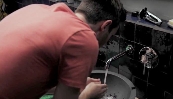 Homme penché sur un lavabo dans la salle de bain pour se laver le visage sous l’eau courante.